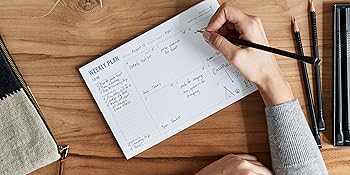 weekly planning pad with to do list and schedule in use on desktop with office supplies